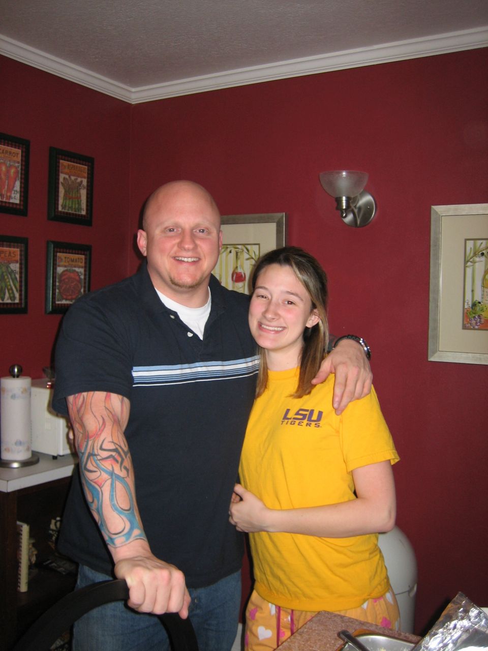 Man with tattooed arm and woman in LSU shirt pose for photo