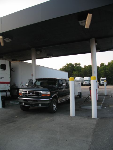 1995 Ford C-350 (Centurion Conversions) - A dark blue 1995 Ford C-350 Centurion Conversions SUV is parked at a gas station, towing a small trailer.
