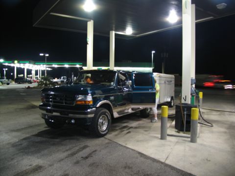 1995 Ford C-350 (Centurion Conversions) - A Ford F-Series truck is parked at a gas station with its door open and a trailer attached.