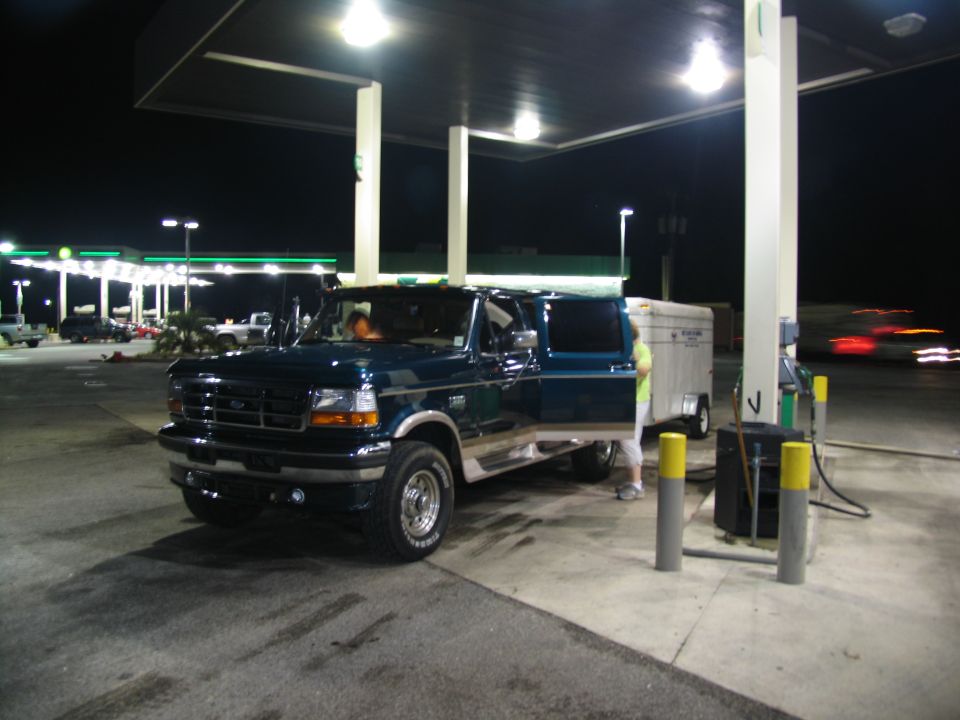 Dark blue Ford F-Series truck with trailer at a gas station at night