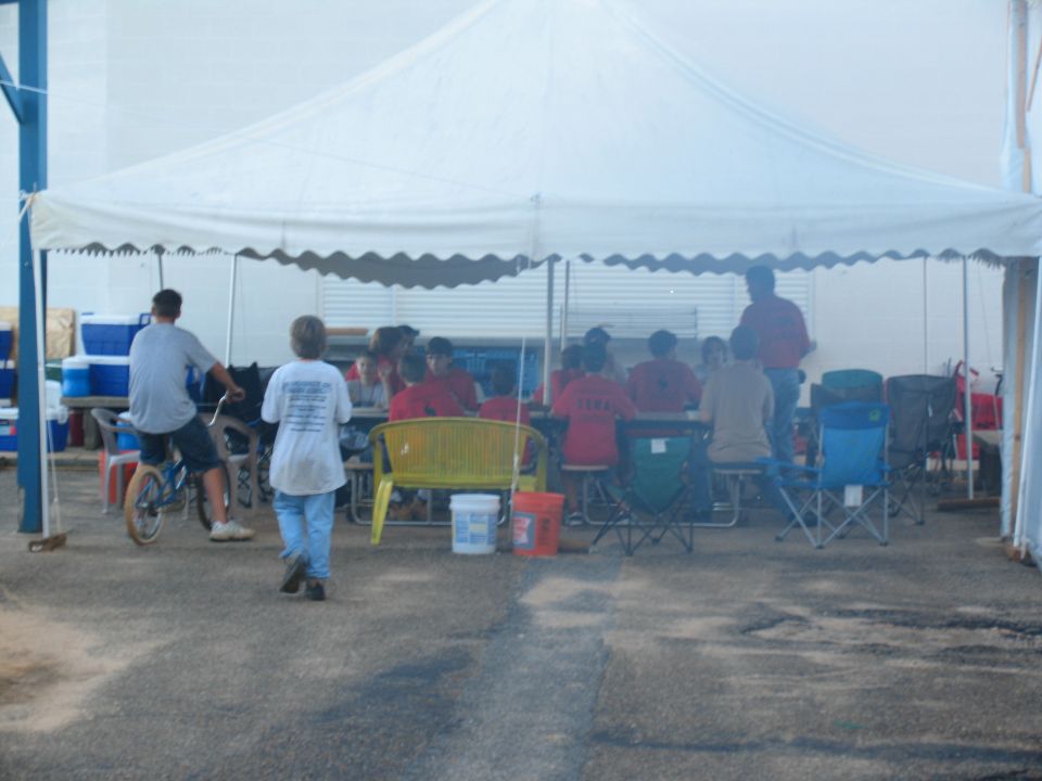 People gathered under a large white tent, some sitting at tables, others standing