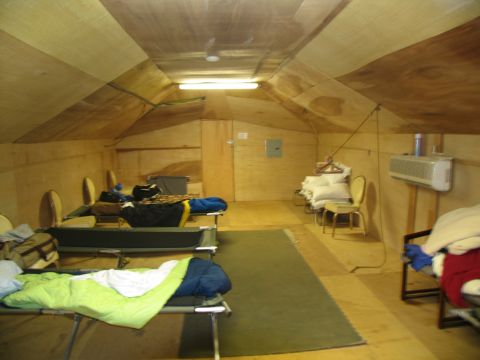 1995 Ford C-350 (Centurion Conversions) - A temporary shelter interior with multiple cots set up for sleeping, along with chairs and personal belongings.