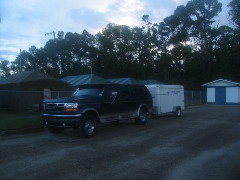 1995 Ford C-350 (Centurion Conversions) - A dark blue Ford Bronco is parked next to a white trailer.