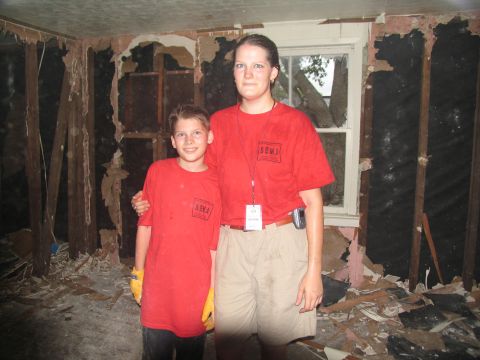 1995 Ford C-350 (Centurion Conversions) - Two individuals in SEMA t-shirts are pictured in a room heavily damaged by what appears to be a natural disaster.