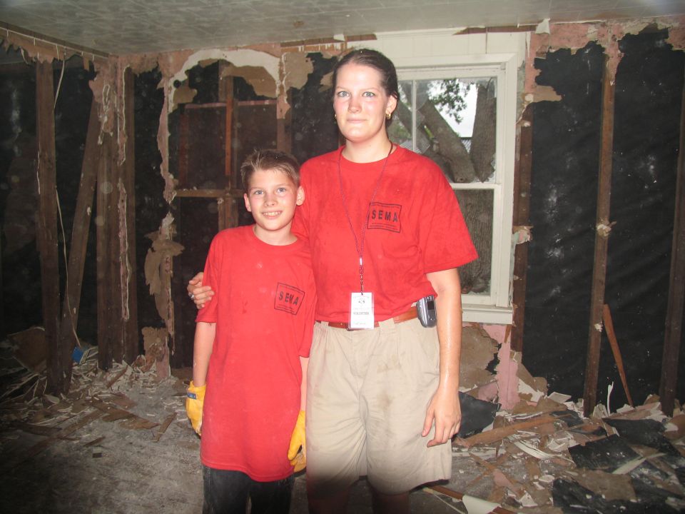 Two people wearing SEMA t-shirts stand in a room with damaged walls and debris