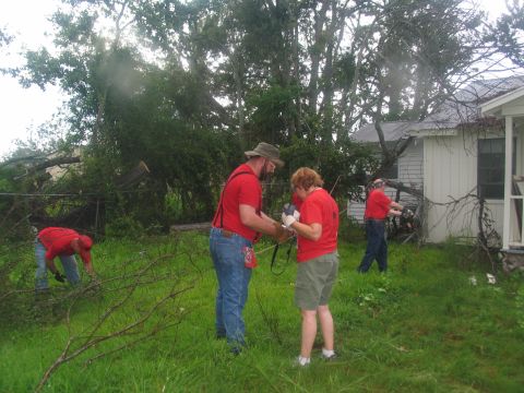 1995 Ford C-350 (Centurion Conversions) - Volunteers work to clear debris after a storm, with a damaged house and fallen trees visible.