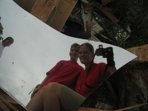 1995 Ford C-350 (Centurion Conversions) - A woman and a boy are reflected in a shiny surface, with debris and foliage visible behind them.
