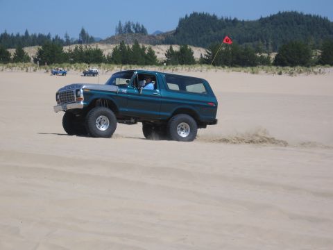 1979 Ford Bronco - A lifted Ford Bronco navigates sandy terrain under a clear blue sky.