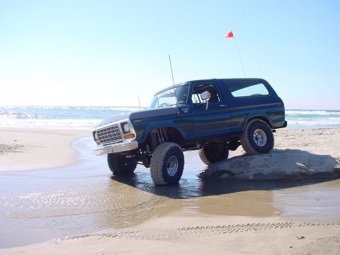 1979 Ford Bronco - Lifted Ford Bronco parked on a beach with the ocean behind it.