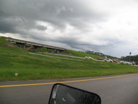 1995 Ford C-350 (Centurion Conversions) - A line of cars travels on a highway as dark storm clouds gather overhead.