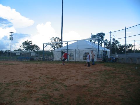 1995 Ford C-350 (Centurion Conversions) - An outdoor scene shows a tent set up on a field, with people engaged in activities and bleachers in the background.