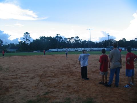 1995 Ford C-350 (Centurion Conversions) - Players and spectators gather on a baseball field during a game.
