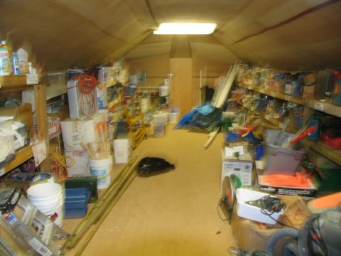 1995 Ford C-350 (Centurion Conversions) - A cluttered storage room contains shelves stocked with containers, buckets, and tools.