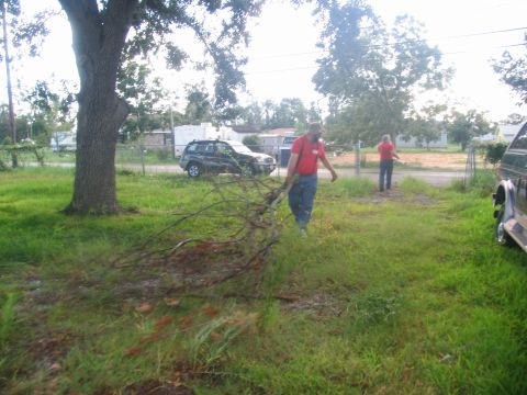 1995 Ford C-350 (Centurion Conversions) - Two individuals are clearing debris from a yard after a storm, with vehicles parked nearby.