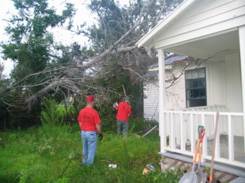 1995 Ford C-350 (Centurion Conversions) - Two men assess damage and clear debris from a yard after a fallen tree impacted a house.