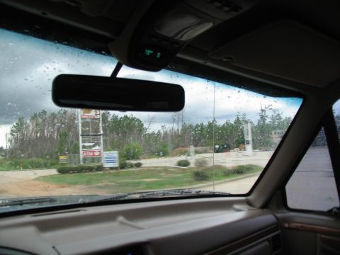 1995 Ford C-350 (Centurion Conversions) - View from inside a vehicle, looking out through a rain-streaked windshield at a gas station and surrounding trees.