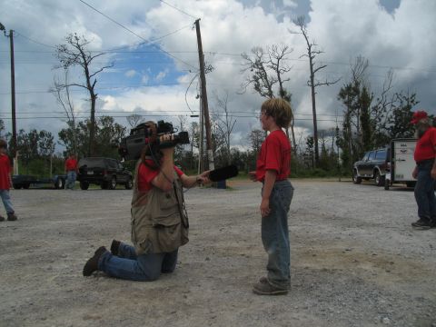 1995 Ford C-350 (Centurion Conversions) - A news crew interviews a child in front of a trailer and two trucks under a cloudy sky.