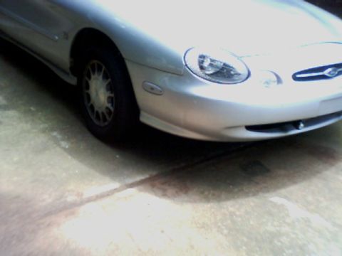1998 Ford Taurus - The front corner of a silver 1998 Ford Taurus is visible, showing its headlight and alloy wheel.