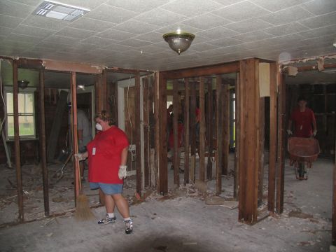 1995 Ford C-350 (Centurion Conversions) - People are cleaning up debris inside a damaged building, with exposed wooden studs and scattered rubble on the floor.