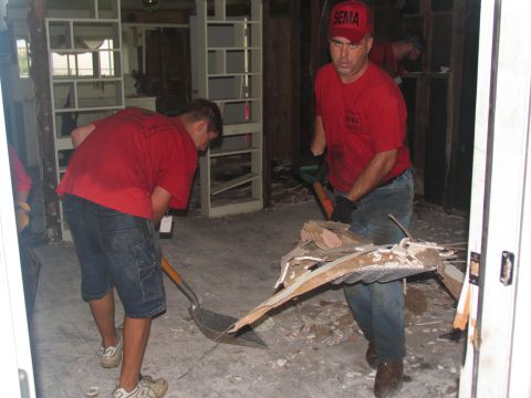 1995 Ford C-350 (Centurion Conversions) - Men in red SEMA shirts clear debris from a room, likely after damage or renovation.