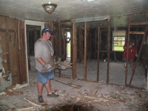 1995 Ford C-350 (Centurion Conversions) - Two individuals are engaged in the process of clearing debris from a damaged interior space, likely after a disaster.