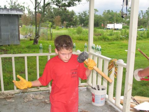 1995 Ford C-350 (Centurion Conversions) - A young boy stands on a porch holding a sledgehammer, wearing yellow gloves and a red shirt.
