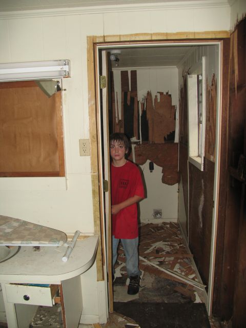 1995 Ford C-350 (Centurion Conversions) - Interior scene of a room with a young boy standing in a doorway, showing signs of damage and debris.