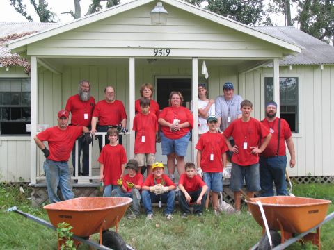 1995 Ford C-350 (Centurion Conversions) - A group of volunteers in red shirts pose for a photo in front of a house, likely during a disaster relief effort.
