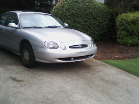 1998 Ford Taurus - A silver sedan is parked outside on a concrete driveway with landscaping in the background.
