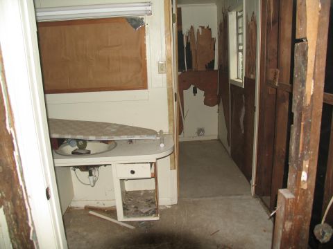 1995 Ford C-350 (Centurion Conversions) - The interior of a room shows significant damage to the walls and flooring, with a sink and ironing board visible.