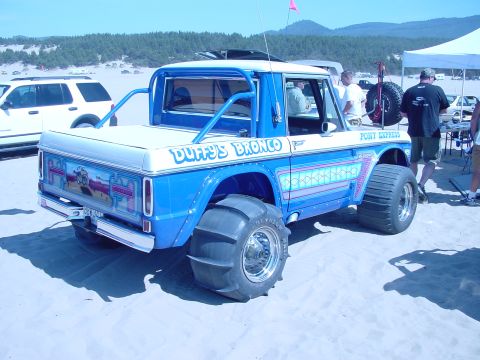 1979 Ford Bronco - Customized 1979 Ford Bronco with sand tires on a beach, with other vehicles and people present.