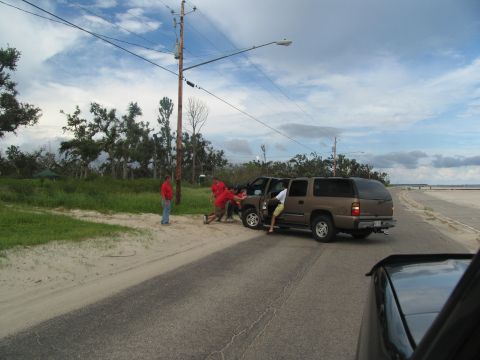 1995 Ford C-350 (Centurion Conversions) - People push a brown SUV on the side of a road under a cloudy sky.
