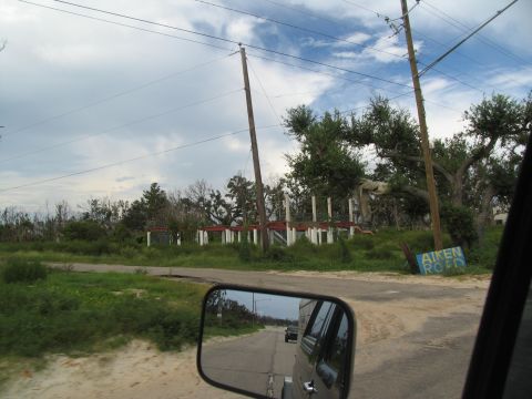 1995 Ford C-350 (Centurion Conversions) - A road sign reads 'AIKEN ROAD' near a damaged building, with a reflection of a vehicle in the side mirror.