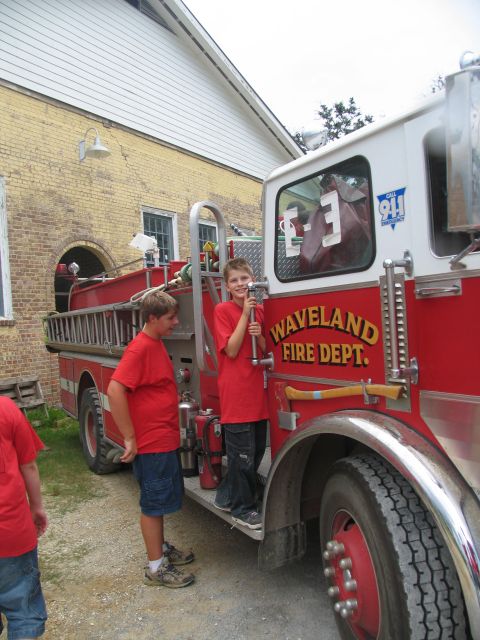 1995 Ford C-350 (Centurion Conversions) - A fire truck with "WAVELAND FIRE DEPT." written on its side is viewed from the side, with two boys standing on its running board.