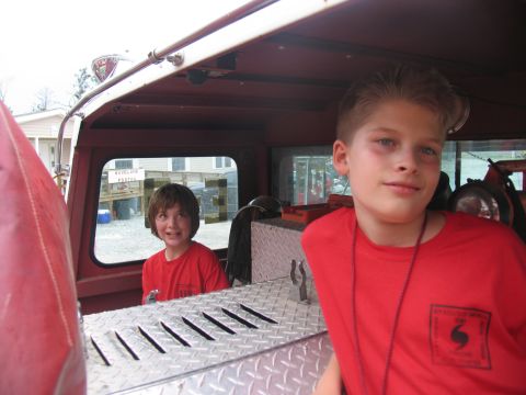 1995 Ford C-350 (Centurion Conversions) - Two boys are inside the cab of a red truck, with one boy looking out the window and the other looking towards the camera.