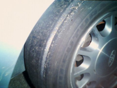 1998 Ford Taurus - Close-up of a worn tire and alloy wheel, showing road debris clinging to the sidewall.