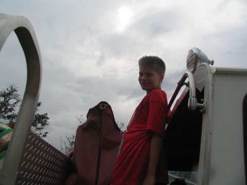 1995 Ford C-350 (Centurion Conversions) - A boy stands on the rear of a white vehicle under a cloudy sky.