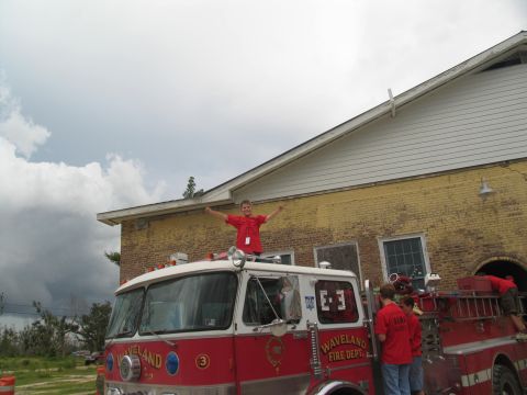 1995 Ford C-350 (Centurion Conversions) - A boy stands on the roof of a Waveland Fire Department truck with his arms wide open, while others gather around the vehicle.