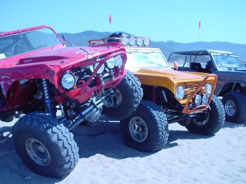 1979 Ford Bronco - Modified Ford Broncos parked on sand dunes under a clear blue sky.