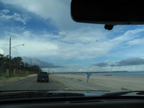 1995 Ford C-350 (Centurion Conversions) - View from inside a vehicle driving down a road beside a sandy beach with the ocean in the distance.