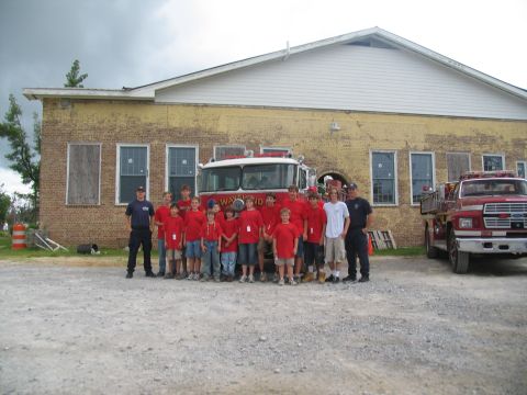 1995 Ford C-350 (Centurion Conversions) - A group of people, likely firefighters or trainees, pose in front of a fire truck outside a building.
