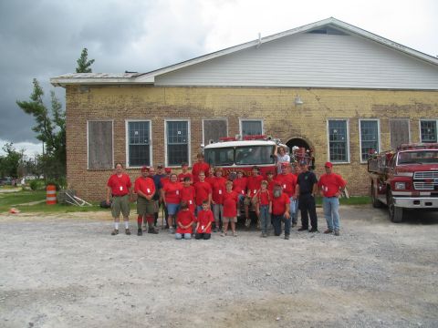 1995 Ford C-350 (Centurion Conversions) - A group of people, some in red shirts, stand in front of a fire truck and a brick building.