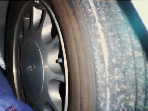 1998 Ford Taurus - A close-up view of the wheel and tire of a 1998 Ford Taurus, highlighting the alloy rim design.