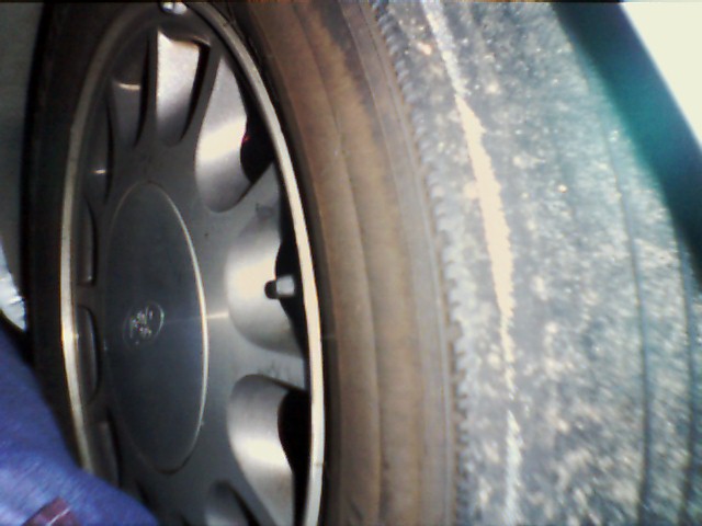Close-up of a 1998 Ford Taurus wheel and tire, showing a silver alloy rim with five spokes and a worn tire tread