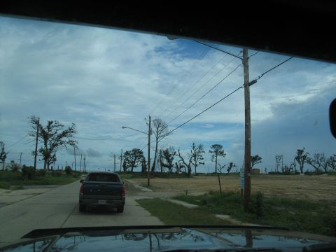 1995 Ford C-350 (Centurion Conversions) - A dark blue pickup truck drives down a road in an area with significant storm damage, including downed trees and power lines.