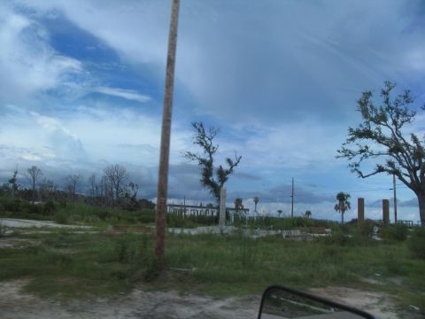 1995 Ford C-350 (Centurion Conversions) - A scene of devastation shows damaged structures and uprooted trees under a dramatic sky, indicative of a recent storm.