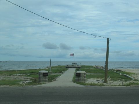 1995 Ford C-350 (Centurion Conversions) - A memorial site with an American flag stands near the ocean on a cloudy day.