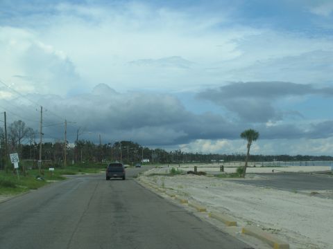 1995 Ford C-350 (Centurion Conversions) - A dark SUV drives down a road with a speed limit sign and storm-damaged trees under a cloudy sky.