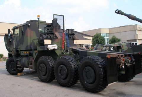 1998 Ford Crown Victoria - Rear three-quarter view of a woodland-camouflage 8x8 military heavy tractor truck on static display in a parking lot, showing twin winch dr…