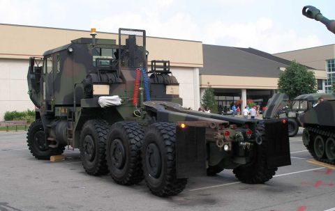 1998 Ford Crown Victoria - Rear three-quarter view of a woodland-camouflage heavy military tractor truck (tank transporter) with multiple axles, a fifth-wheel flatbed…